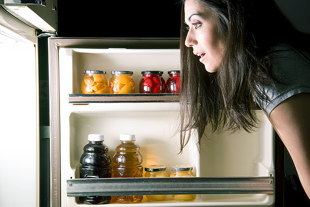 Woman standing in front of a refrigerator at night.